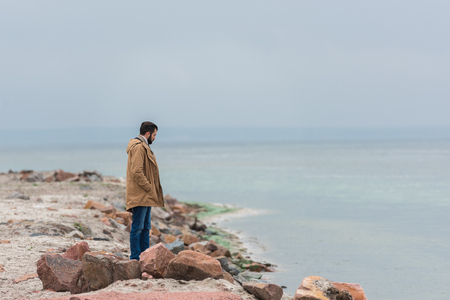 lonely sad man standing on rocky seashoreの写真素材