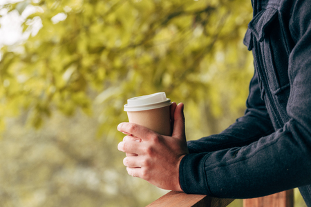 cropped shot of young man holding disposable coffee cup in autumn parkの写真素材