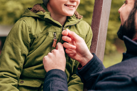 cropped shot of father fastening jacket of cute smiling little son in parkの写真素材