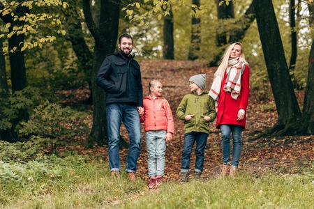 happy young family smiling at camera while walking together in autumn park