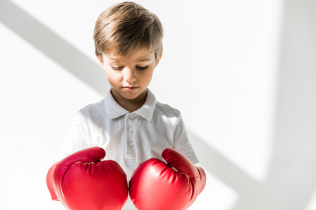 cute little boy in boxing gloves looking down on white