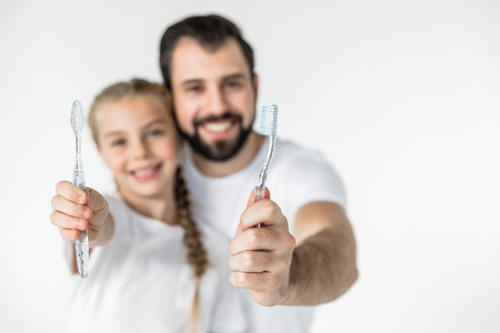 close-up view of happy father and daughter holding toothbrushes isolated on whiteの写真素材