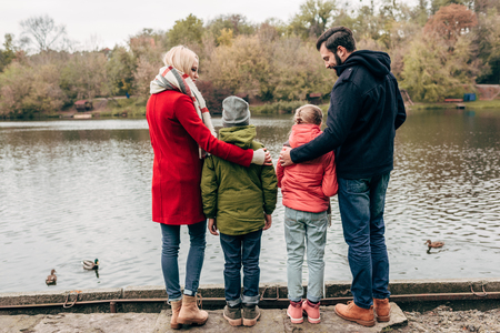 back view of young family with two kids looking at lake in autumn parkの写真素材