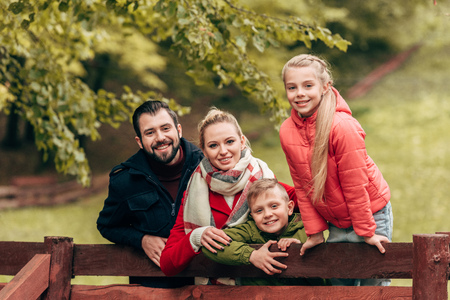 happy family leaning at wooden fence and smiling at camera in autumn parkの写真素材