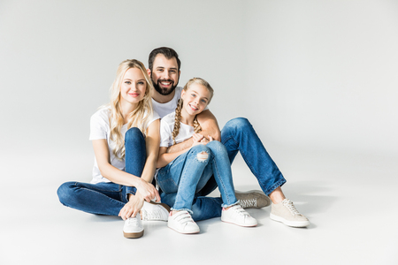 cheerful parents with happy daughter sitting together and smiling at camera isolated on whiteの写真素材