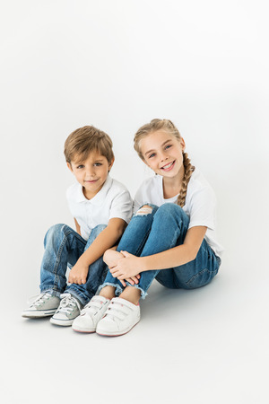 adorable little children sitting together and smiling at camera isolated on whiteの写真素材