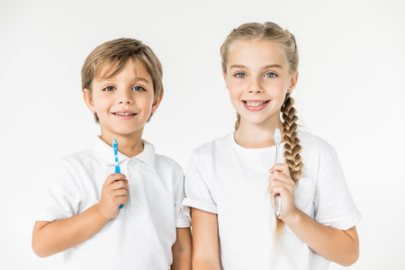 kids holding toothbrushes and smiling at camera isolated on white