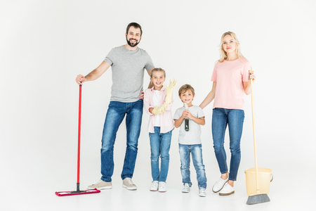 happy young family with cleaning equipment smiling at camera isolated on whiteの写真素材