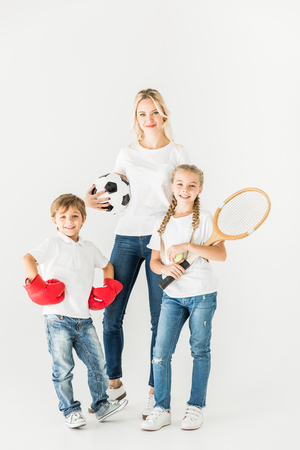happy mother and kids holding sport equipment and smiling at camera isolated on whiteの写真素材