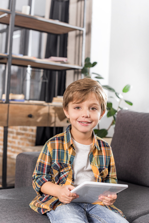 portrait of smiling little boy with tablet in hands looking at camera at homeの写真素材