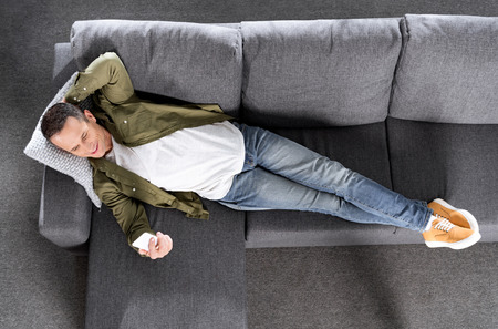 top view of man using smartphone while laying on couchの写真素材