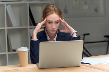 pensive woman sitting at table against laptop  and coffe in cupの写真素材