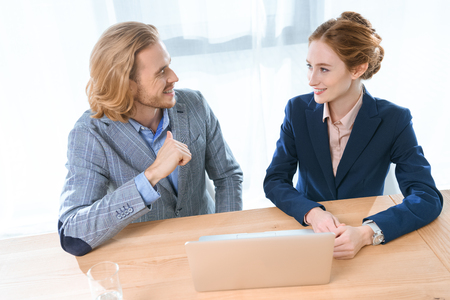 businesspeople smiling to each other while sitting at table with laptop の写真素材