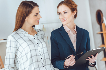 smiling businesswomen talking in office and looking at each otherの写真素材