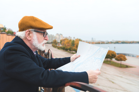 bearded senior man in cap looking at map の写真素材