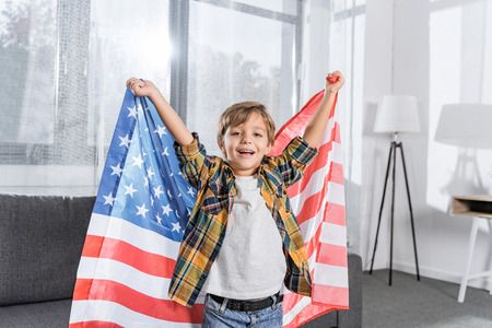 portrait of happy little boy with american flag in hands looking at camera at homeの写真素材