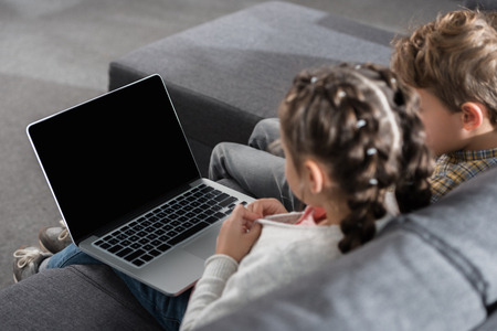 Preschooler female and male kids sitting on a sofa with a laptopの写真素材