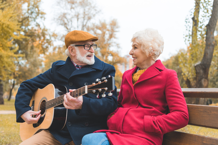 happy senior couple playing on acoustic guitar in autumn parkの写真素材