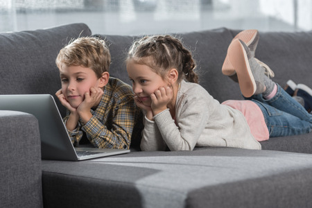 Preschooler children lying on a sofa with a laptop の写真素材