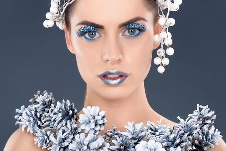 portrait of beautiful girl with hair accessory, christmas pine cones, winter makeup and glitter, isolated on greyの写真素材
