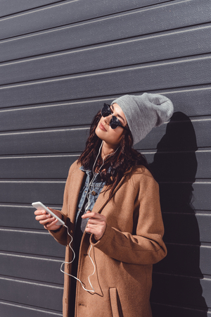 beautiful woman in autumn outfit and black sunglasses listening to music with smartphone outsideの写真素材