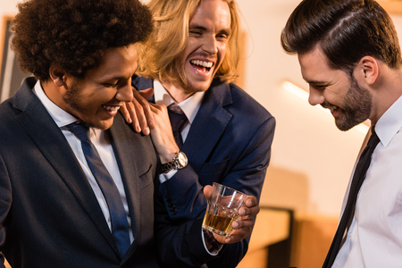 three multiethnic businessmen laughing while drinking whiskey in barの写真素材