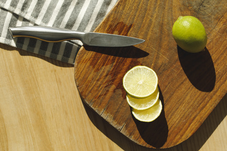 top view of limes and knife on wooden board on tableの写真素材