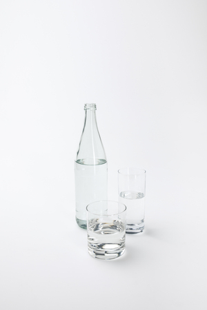 two different glasses and bottle with calm water isolated on white の写真素材