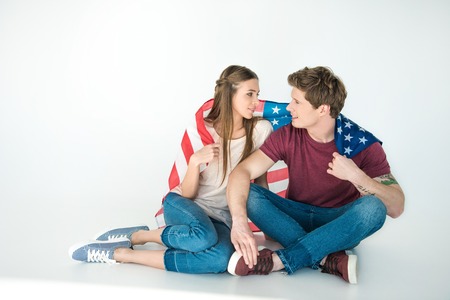 happy young couple holding american flag and smiling each other on greyの写真素材