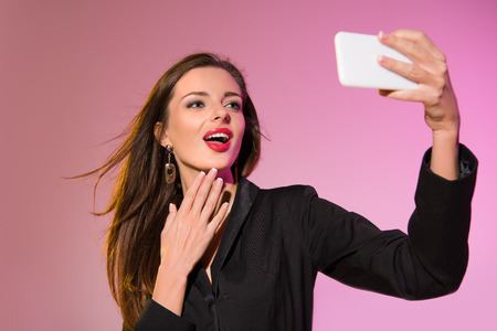 stylish attractive woman taking selfie on smartphone, isolated on pink