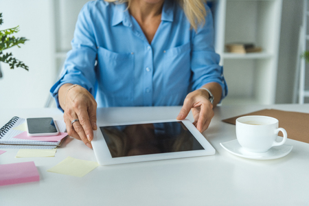 cropped view of businesswoman with cup of coffee using tablet with blank screenの写真素材