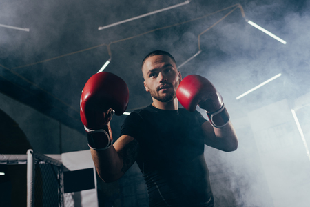 low angle view of muscular young sportsman in boxing gloves training in sport clubの写真素材