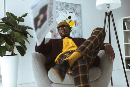 stylish african american businessman sitting in armchair and throwing business newspaper  の写真素材