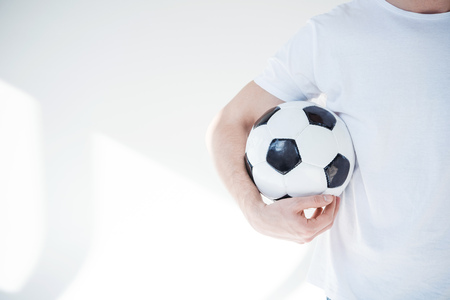 cropped shot of young man holding soccer ball on grey