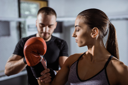 selective focus of male trainer wrapping boxing glove to beautiful young sportswomanの写真素材