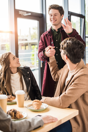 Man shaking hand to friend and waving hand to girlsの写真素材
