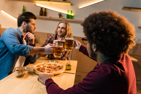 young multiethnic friends drinking beer and eating pizza in barの写真素材