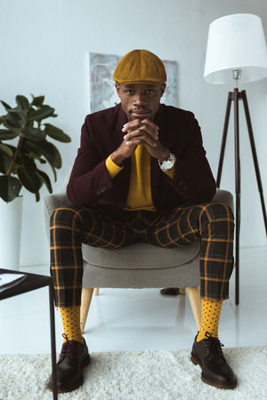 pensive fashionable african american man sitting in armchair in modern officeの写真素材