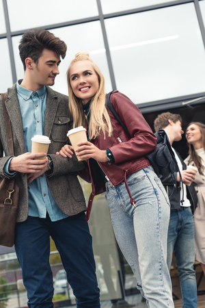 Two heterosexual couples going out from building with coffee in paper cupsの写真素材