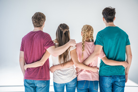 back view of young people embracing while standing together on greyの写真素材