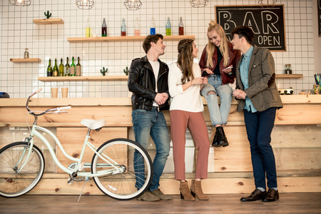 Four female and male friends talking and standing at bar counter 