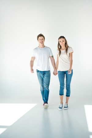 happy young couple holding hands and walking together on greyの写真素材