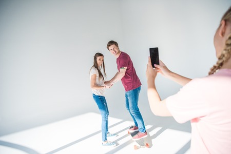 cropped shot of girl photographing happy young couple on smartphone on greyの写真素材