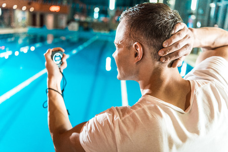 handsome swim trainer with timer standing at competition swimming poolの写真素材