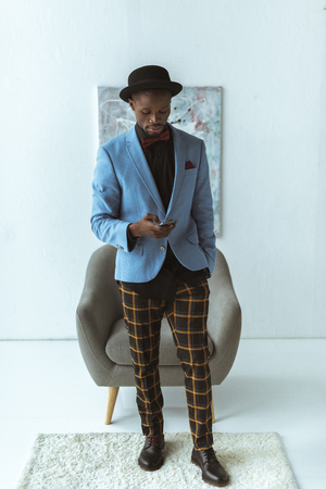 fashionable african american man in checkered pants and blue jacket using smartphoneの写真素材