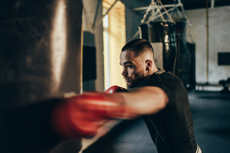 selective focus of young sportsman in boxing gloves training with punching bagの写真素材