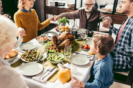 beautiful religious family holding hands and praying on thanksgiving before holiday dinnerの写真素材