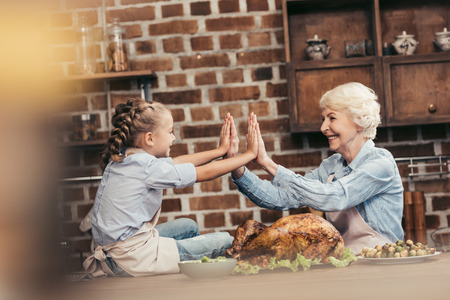 grandmother and granddaughter giving double high five on thanksgiving after successful turkey cookingの写真素材