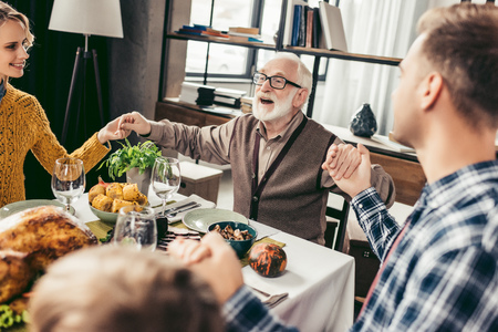 happy christian family praying before holiday dinner and holding handsの写真素材