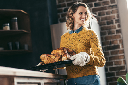 young beautiful woman carrying tray with delicious turkey for thanksgiving dinnerの写真素材